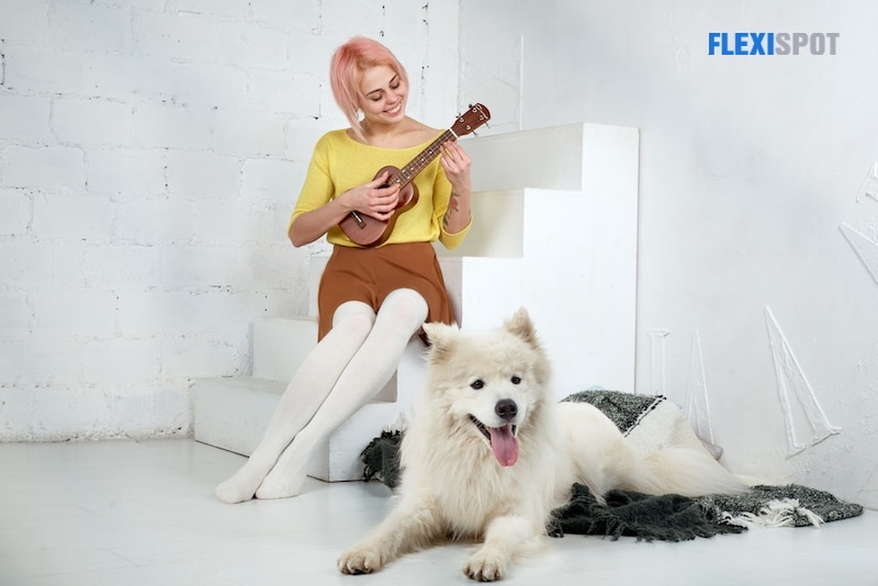 Young smiling woman girl in skirt and blouse, playing the ukulele, sitting on the steps with a smile on her face