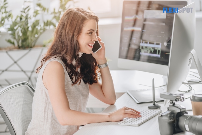 Side view of happy editor talking on smartphone near computer monitor