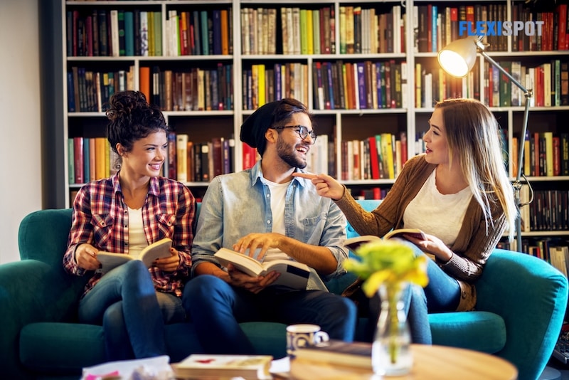 Three happy young friends studying in library discussing notes