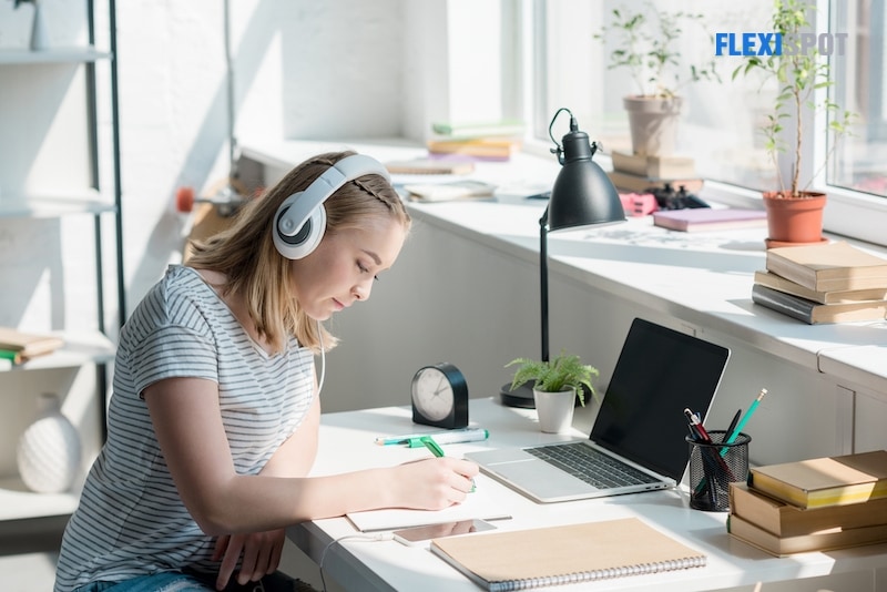 Teen student girl listening music with headphones and doing homework