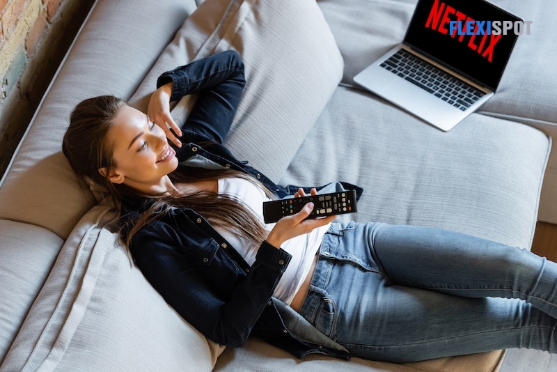 overhead view of happy woman holding remote controller near laptop with netflix website on sofa
