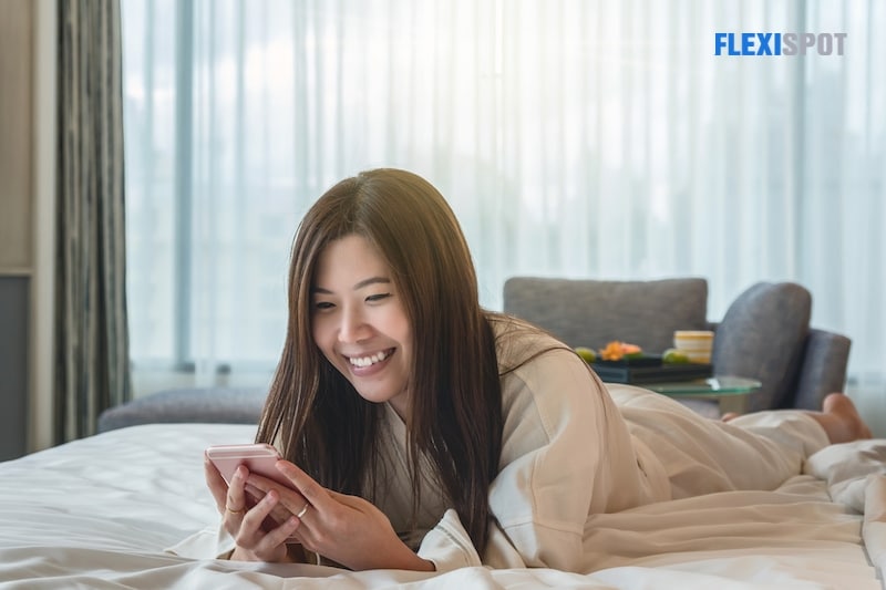 Lifestyle portrait of young happy and pretty Asian Korean woman at home bedroom or hotel room lying on bed relaxed smiling cheerful using internet online dating app texting on mobile phone
