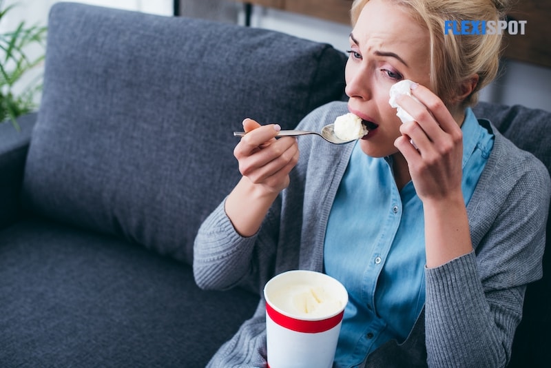 Woman eating ice cream and crying while sitting on couch at home alone