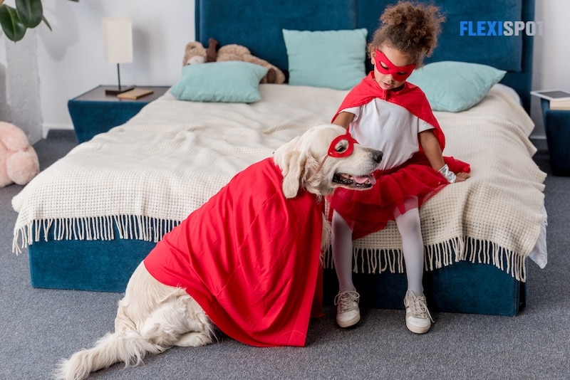Adorable little african american kid playing with dog in superhero costumes in bedroom