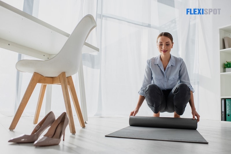 Happy young businesswoman laying yoga mat on floor in office