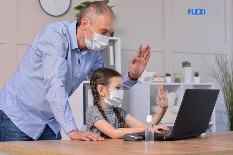 Happy father and daughter in medical masks greet with friends or teacher via laptop during coronavirus pandemic. Online communication, training, social distance, stay at home, homeschooling concept