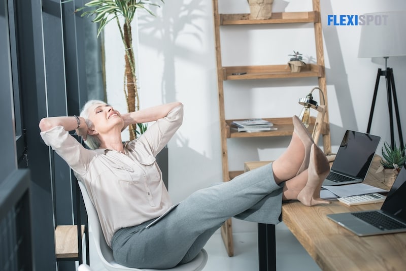 Happy tired businesswoman stretching arms in modern office