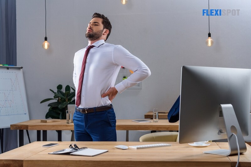 Tired businessman standing and stretching in the office