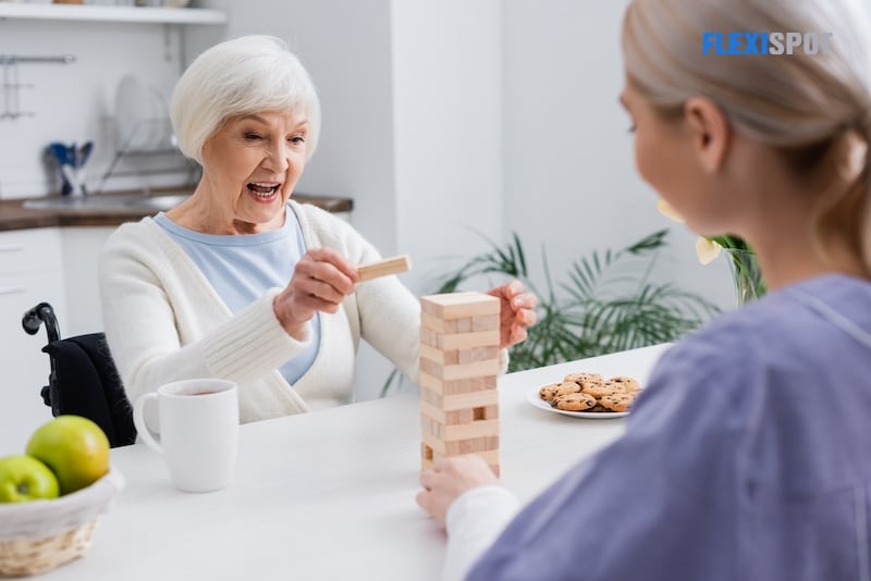 Excited senior woman playing wooden tower game with social worker on blurred foreground